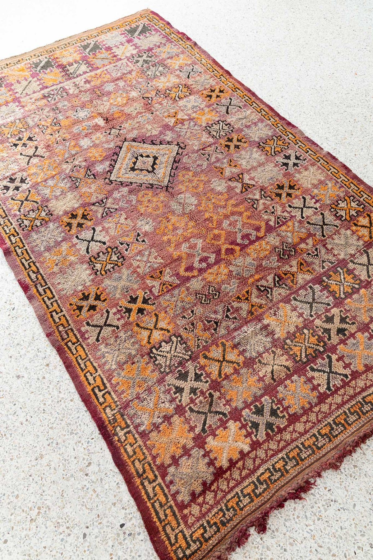 This vintage Moroccan rug is a true masterpiece, with its intricate patterns and beautiful color palette. It may come from a Boujaad, Ait Yacoub or Zemmour tribe. The carpet is a real feast for the eyes, with a mixture of colors and Berber signs in a sophisticated and elegant composition. The design is dense and intricate, with a symmetrical pattern that has variations in the organization of the composition. Faded color palette from rosy to orange, beige and dark.